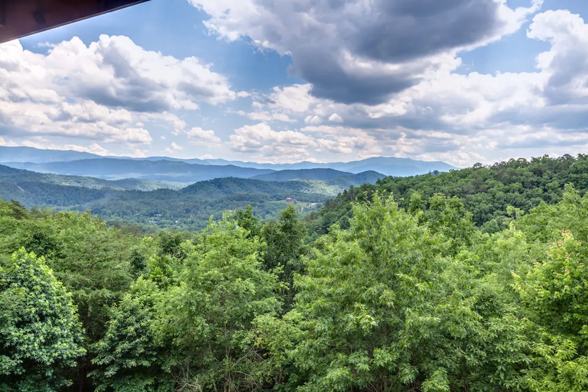 A panoramic view of a Smoky Mountain range blanketed in dense greenery stretches beneath a soft, cloudy sky. The scene evokes the beauty and grandeur of the natural environment, encouraging exploration and outdoor adventures for families.