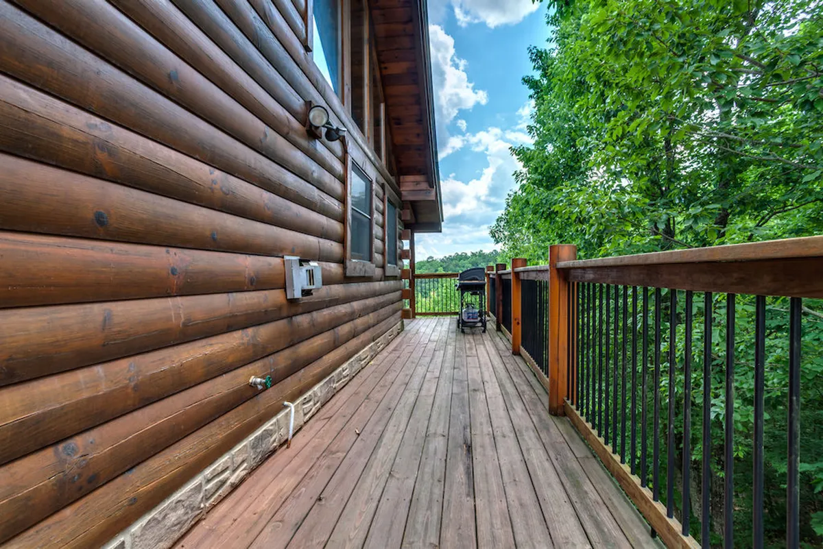 A serene wooden deck lined with logs from the cabin, surrounded by trees. The space is ideal for outdoor relaxation, socializing, and taking in the natural ambiance. This deck represents a central gathering spot for evening hangouts, BBQs, or simply admiring mountain sunsets.