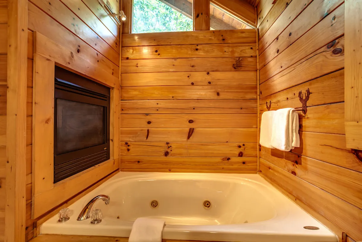 A tranquil bathroom with a soaking tub positioned beside a fireplace, set against wooden walls and complemented by plush towels. The ambiance is inviting and spa-like, perfect for relaxation and indulgence.