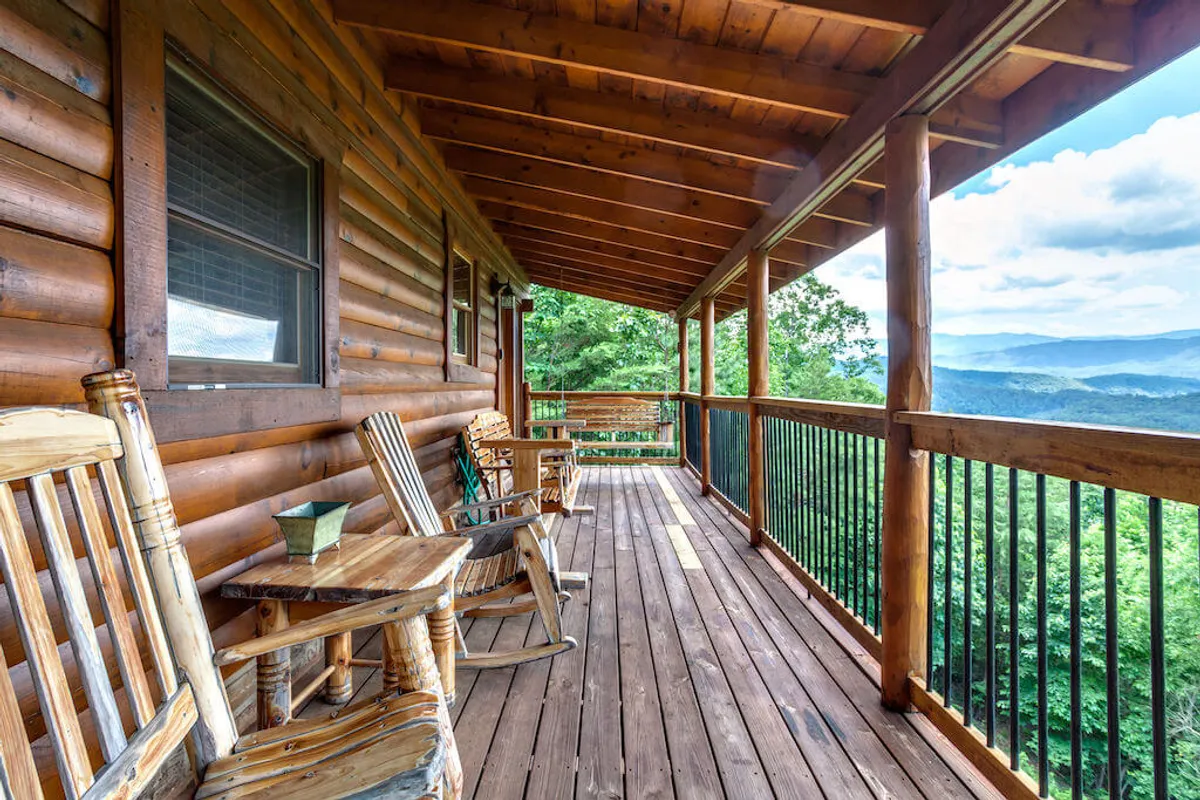 This exterior image showcases a rustic wooden porch outfitted with classic rocking chairs and a sturdy railing, with breathtaking Smoky Mountain vistas stretching into the distance. The tranquil scene invites guests to relax, enjoy a sunrise coffee, or spend an evening stargazing surrounded by the sounds of nature.