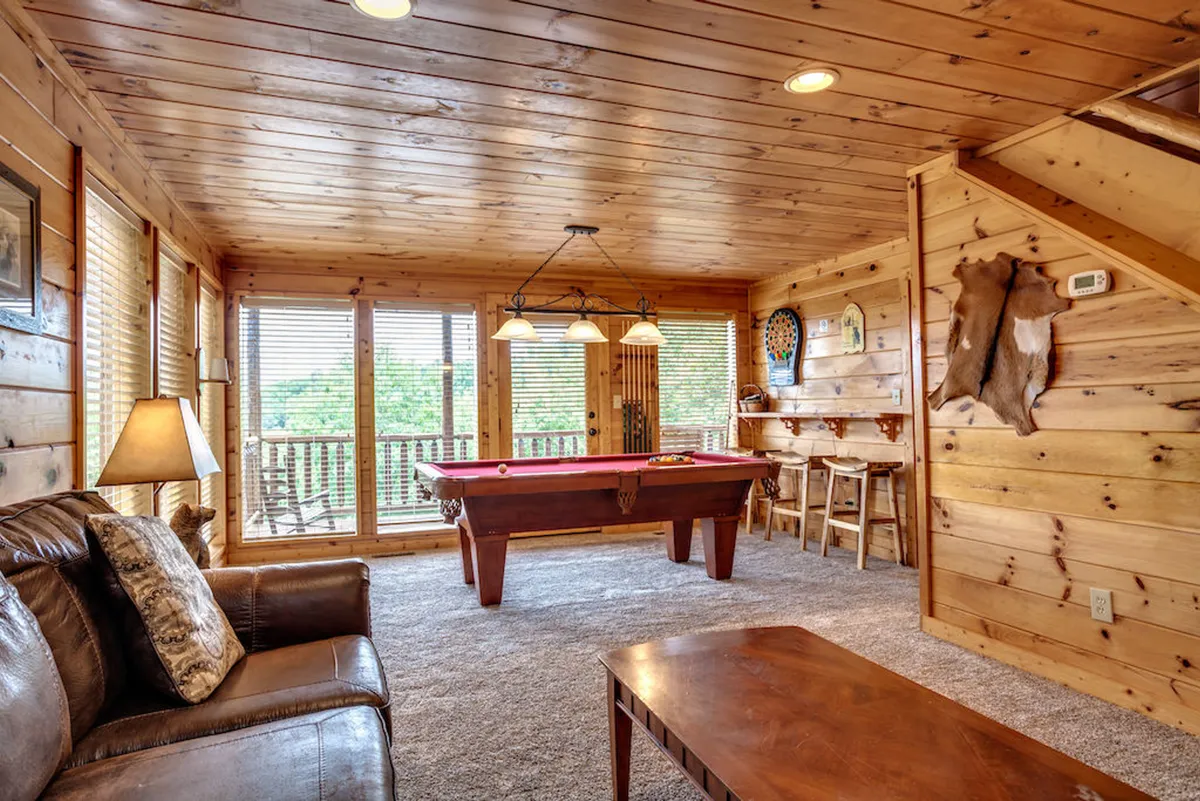 A spacious game room with a pool table, cozy sofa, and large windows that let in plenty of natural light. The warm wood interior creates a fun and inviting atmosphere for families to unwind and reconnect after a day out.