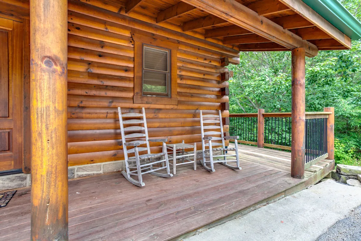 This exterior image highlights classic wooden rocking chairs on a log cabin porch, surrounded by lush greenery. The peaceful scene suggests relaxation after an active day outdoors, blending comfort with a strong connection to nature.