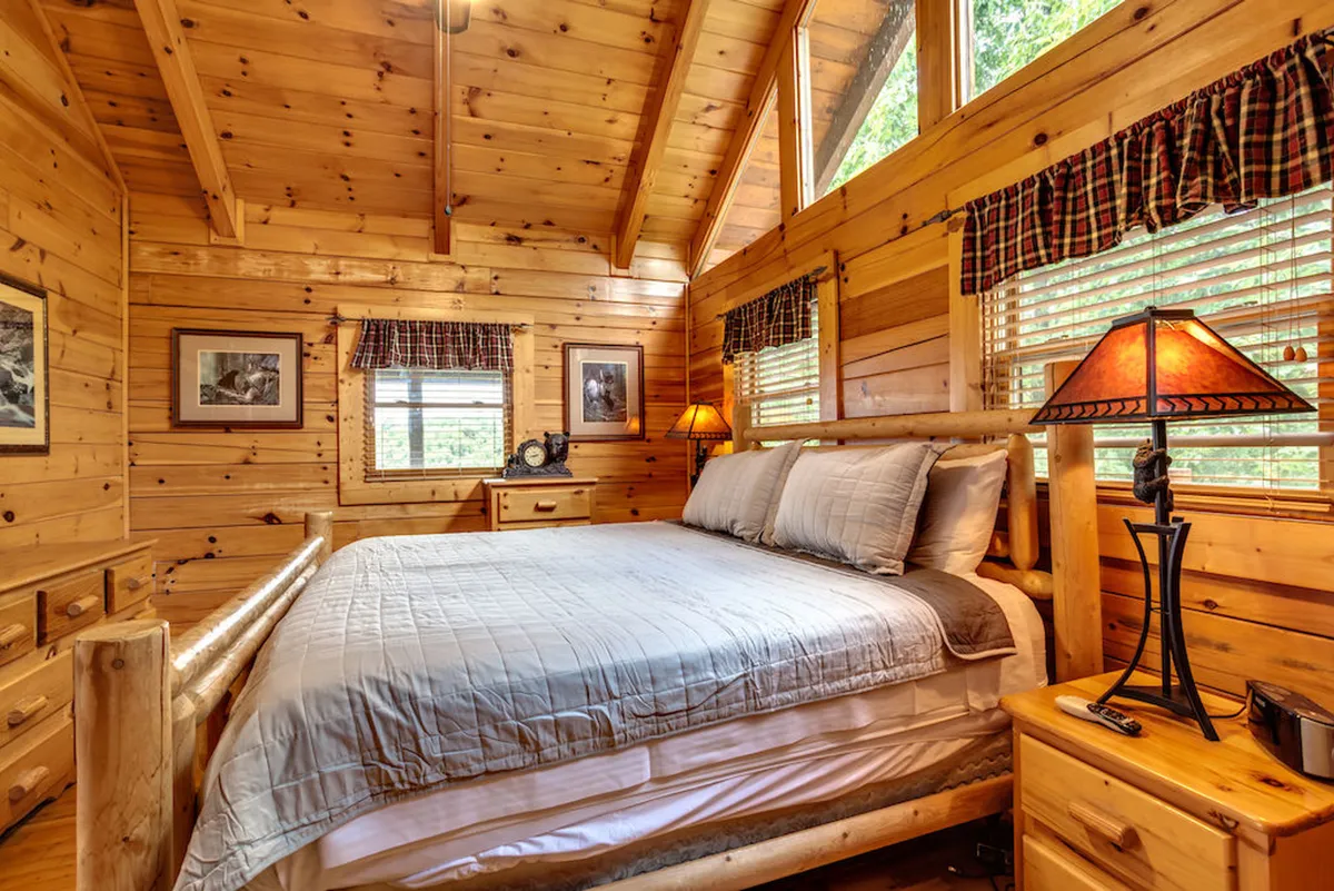 A serene king-sized log bed surrounded by wooden furniture and soft lamp lighting. The space is tranquil and bathed in natural light, suggesting fresh linens and peaceful, restful sleep.