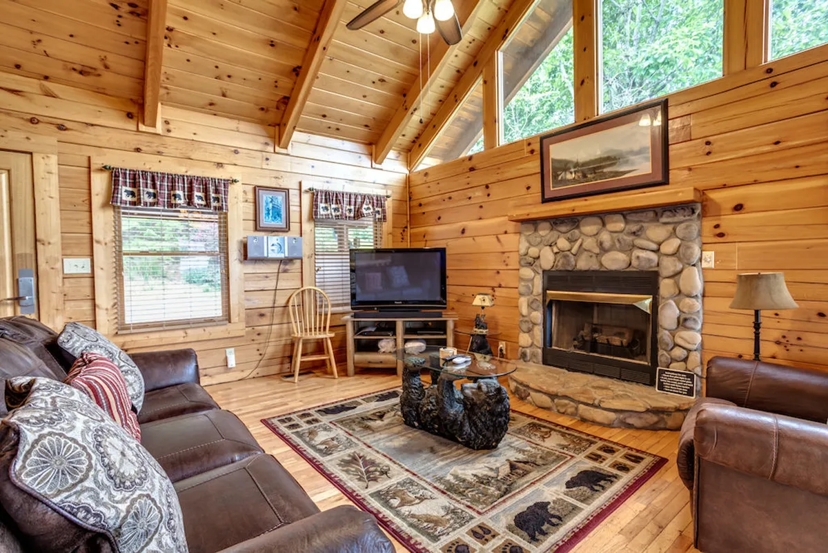 This image features a cozy living room with a gas fireplace as the focal point. Large windows allow sunlight to pour into the space, illuminating a comfortable seating area centered around a coffee table adorned with decorative items. The arrangement is ideal for gatherings, reading, or movie nights.