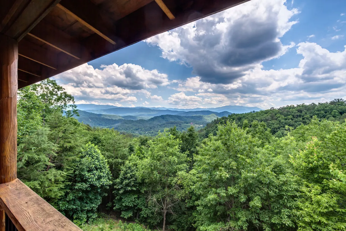 A dramatic mountain range unfolds in the distance, with dense greenery and a sky brimming with clouds. The view is panoramic, evoking a sense of awe and providing a perfect setting for sunrise yoga, group meals, or simple contemplation.